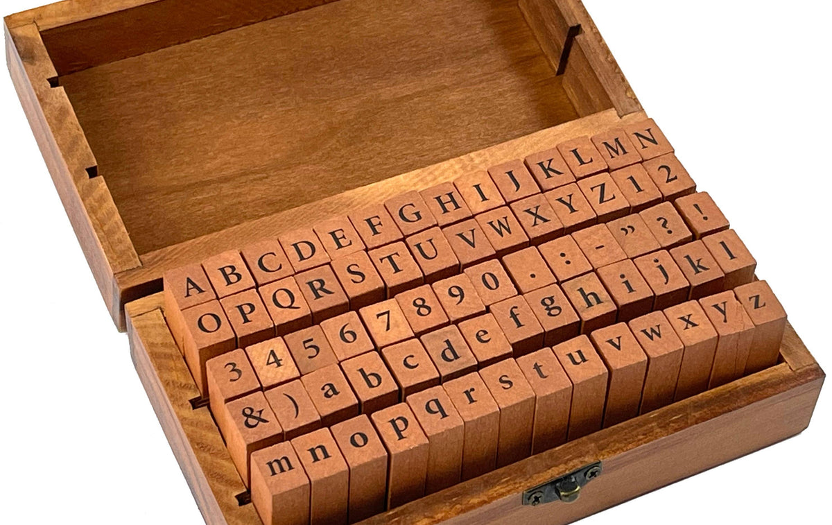 A wooden box with an open lid displays alphabet and number rubber stamps. The orderly arrangement conveys a sense of organization and creativity.