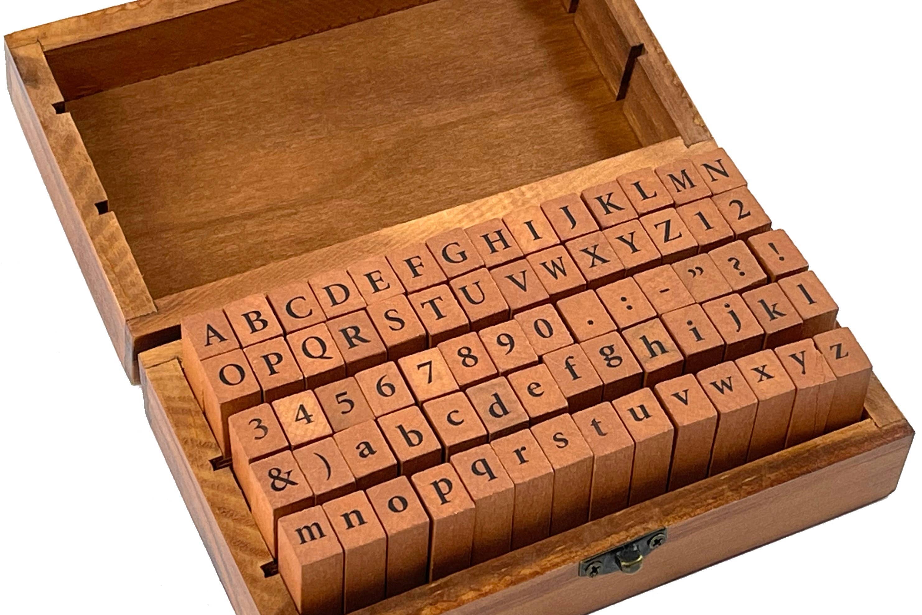 A wooden box with an open lid displays alphabet and number rubber stamps. The orderly arrangement conveys a sense of organization and creativity.