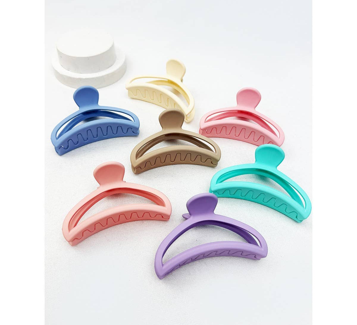 An assortment of seven minimalist matte half moon hair claw clips in a variety of pastel and muted tones, including coral, lavender, turquoise, and tan, arranged neatly together.