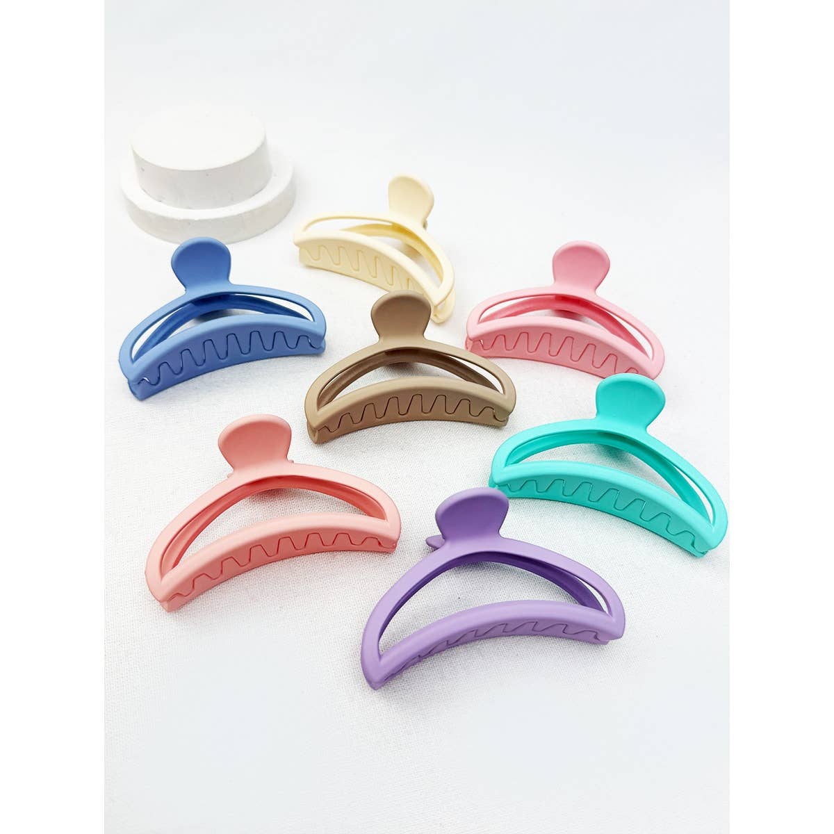 An assortment of seven minimalist matte half moon hair claw clips in a variety of pastel and muted tones, including coral, lavender, turquoise, and tan, arranged neatly together.