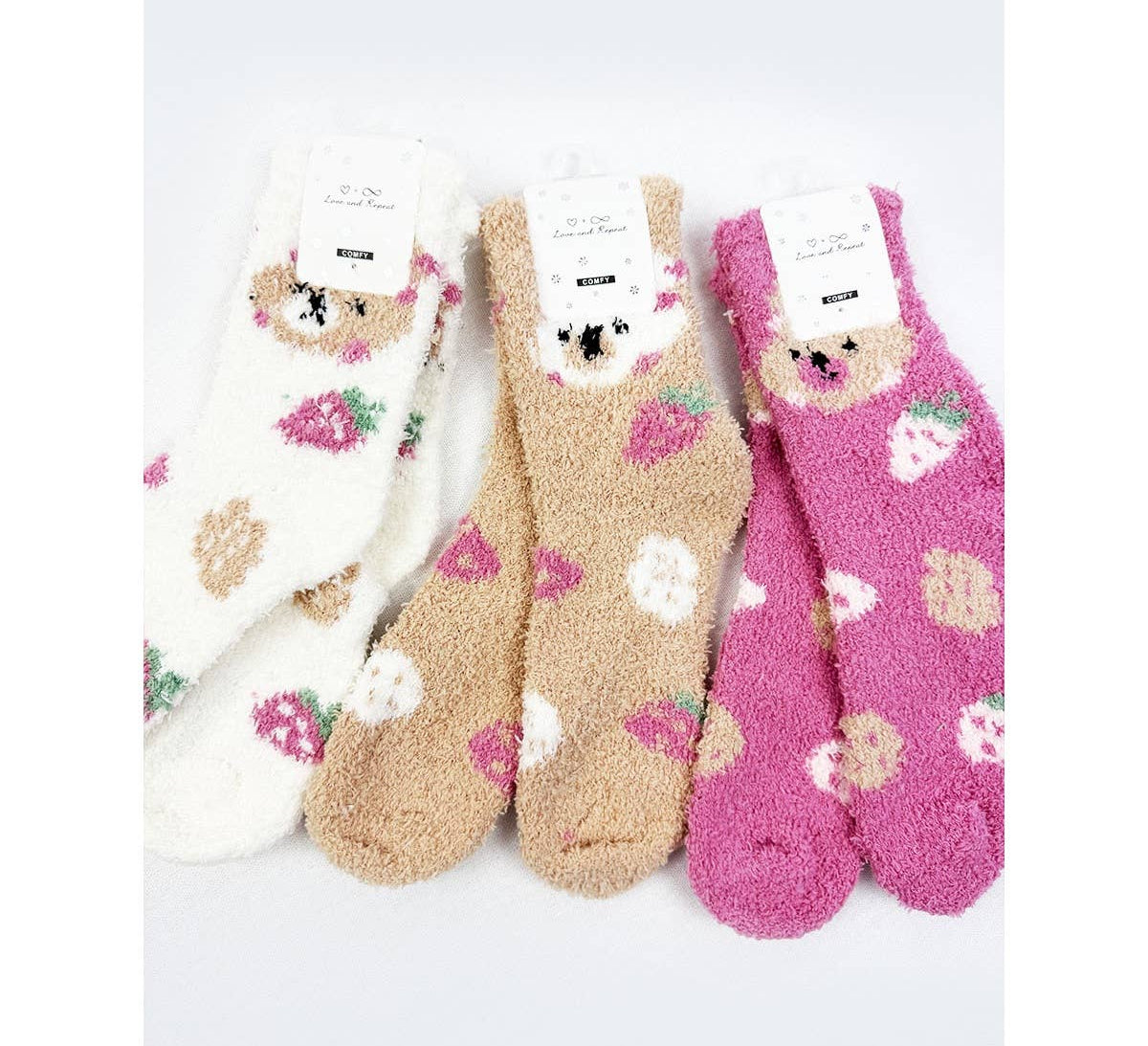 Three pairs of fuzzy, plush crew socks in white, light brown, and dark pink, featuring an embroidered bear face at the top cuff and a strawberry pattern.