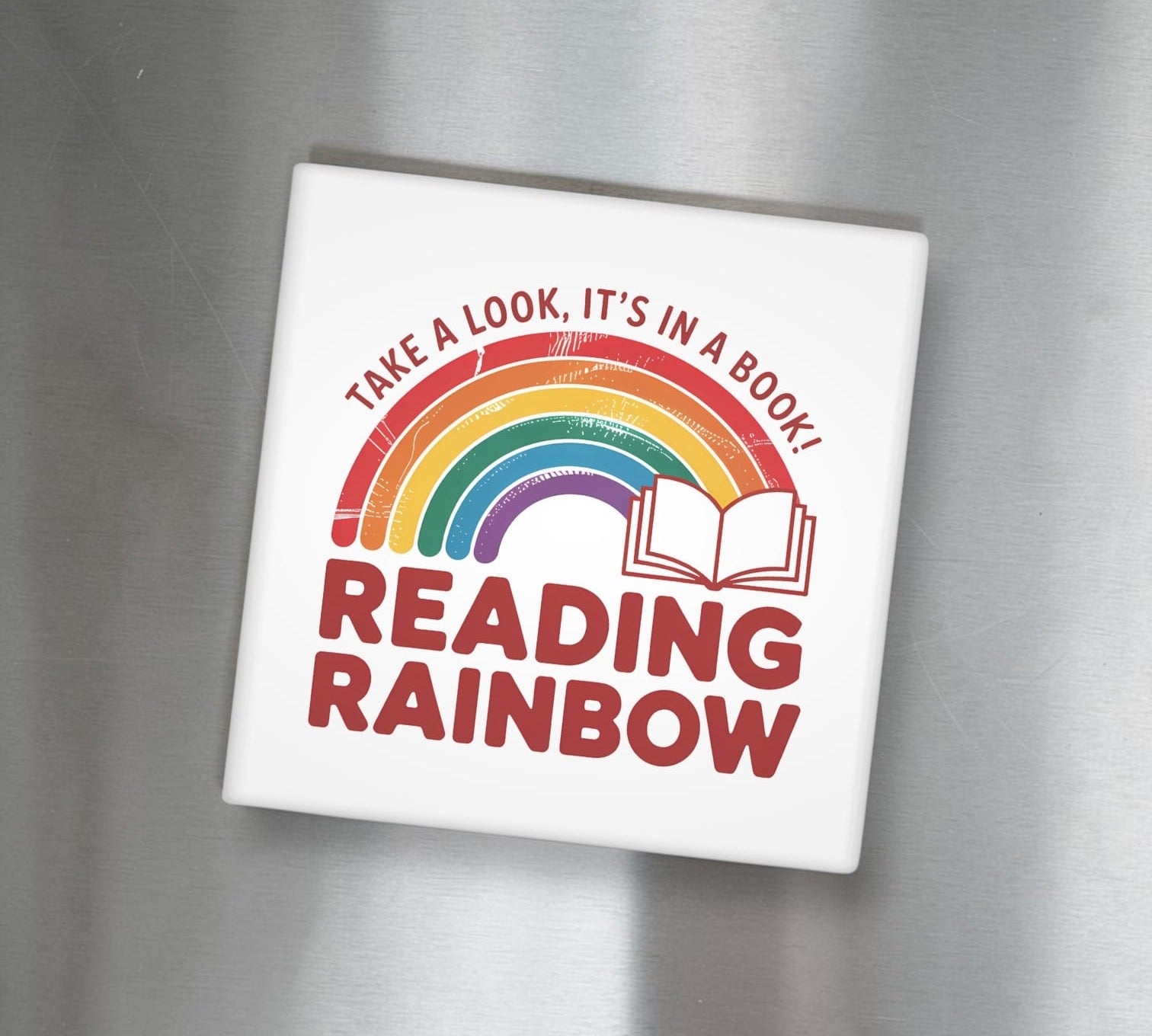 White square magnet with rainbow and text on a metallic surface - Take a Look It's In a Book Reading Rainbow"