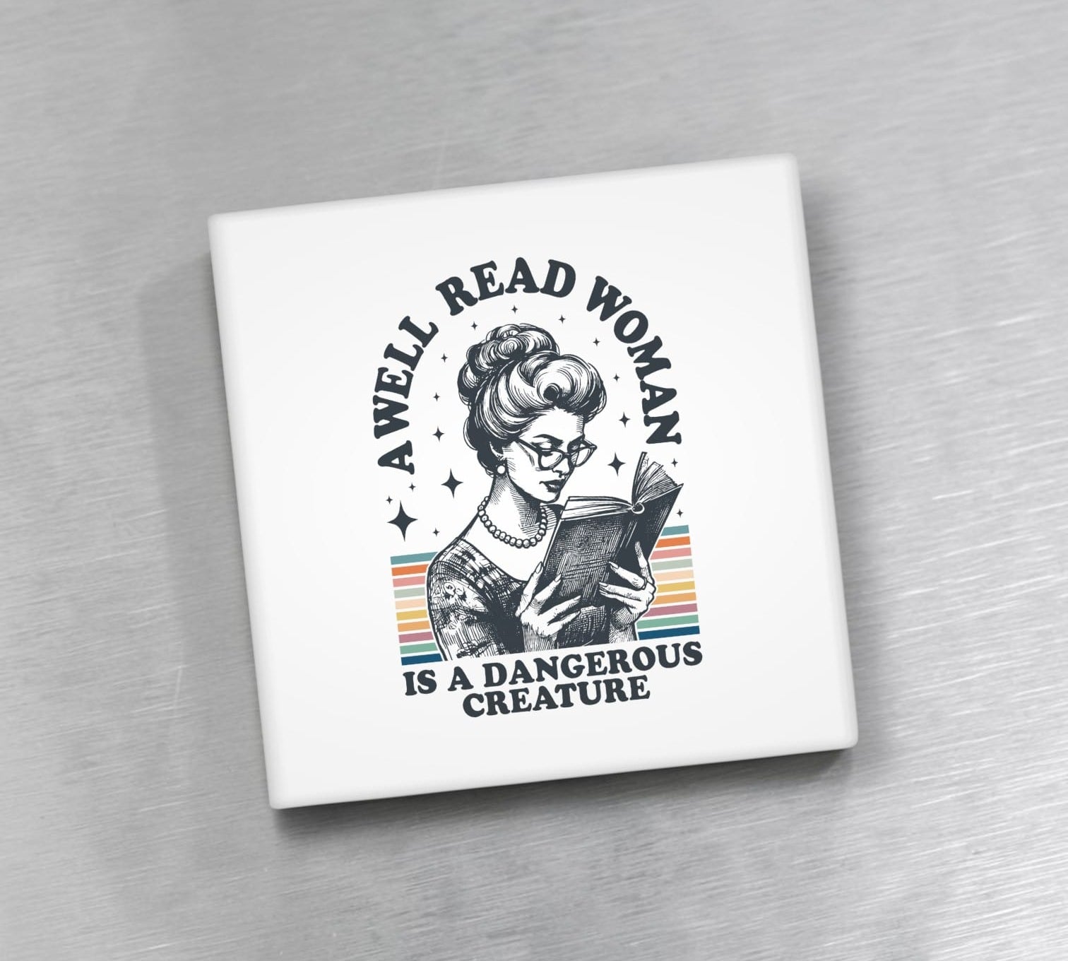 Square magnet with a graphic of a woman reading a book and text 'A well-read woman is a dangerous creature' on a gray background.