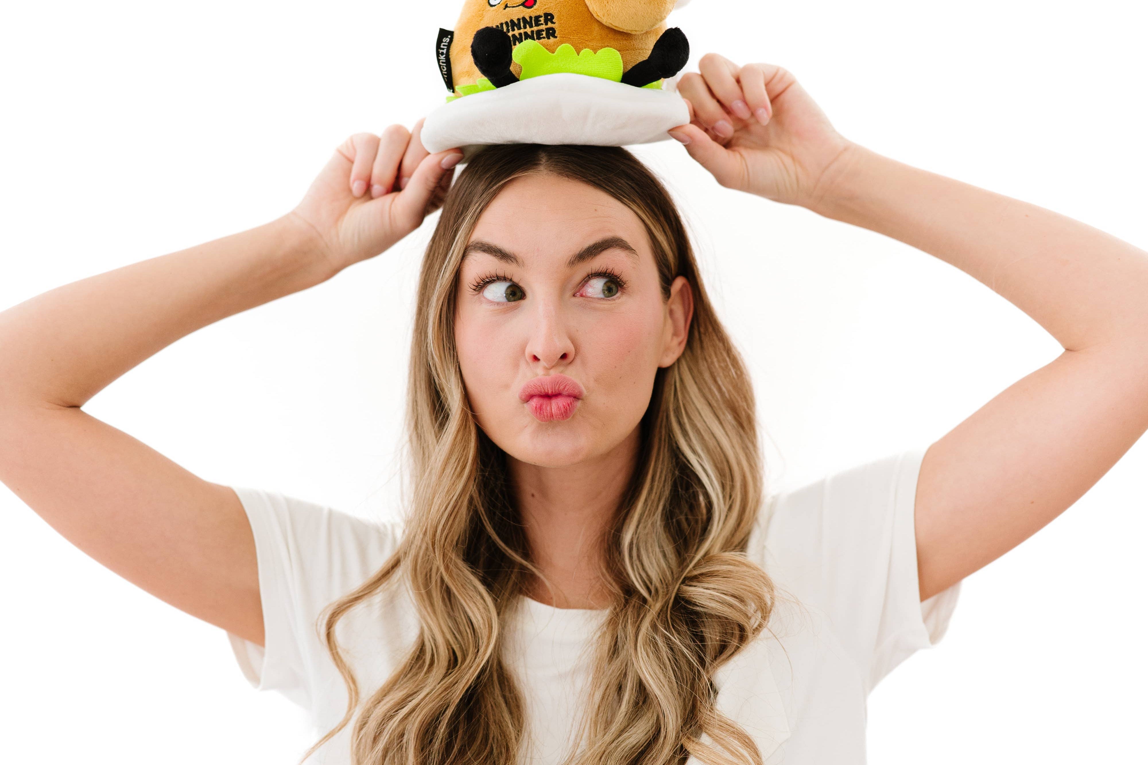 Woman holding on top of her head a A cooked turkey dinner plush on a plate with green lettuce. The turkey has a smiley face with a red tongue sticking out and black text that says "Winner Winner." It also has black legs sticking out.