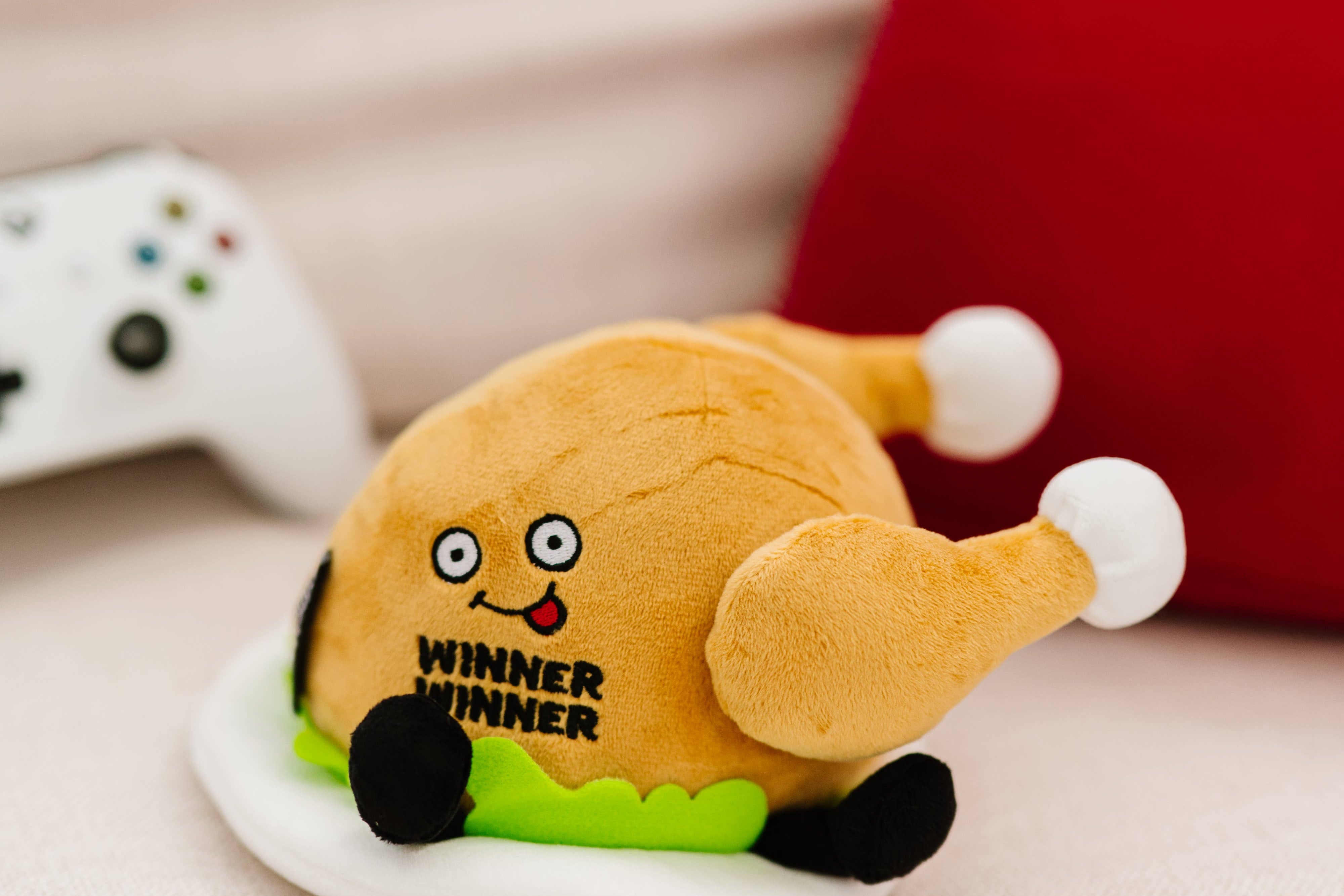 A cooked turkey dinner plush on a plate with green lettuce. The turkey has a smiley face with a red tongue sticking out and black text that says "Winner Winner." It also has black legs sticking out.