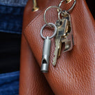 Keychain with keys and a whistle attached to a brown leather bag.