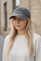 Woman wearing a gray 'OFF DA' cap outdoors with a blurred building background