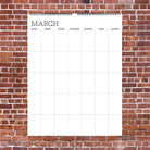 A blank March calendar is displayed on a red brick wall. The calendar is empty with grid lines for each day of the week, conveying a sense of anticipation.