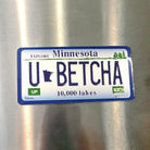 Minnesota-themed license plate sticker with 'U BETCHA' on a metallic surface