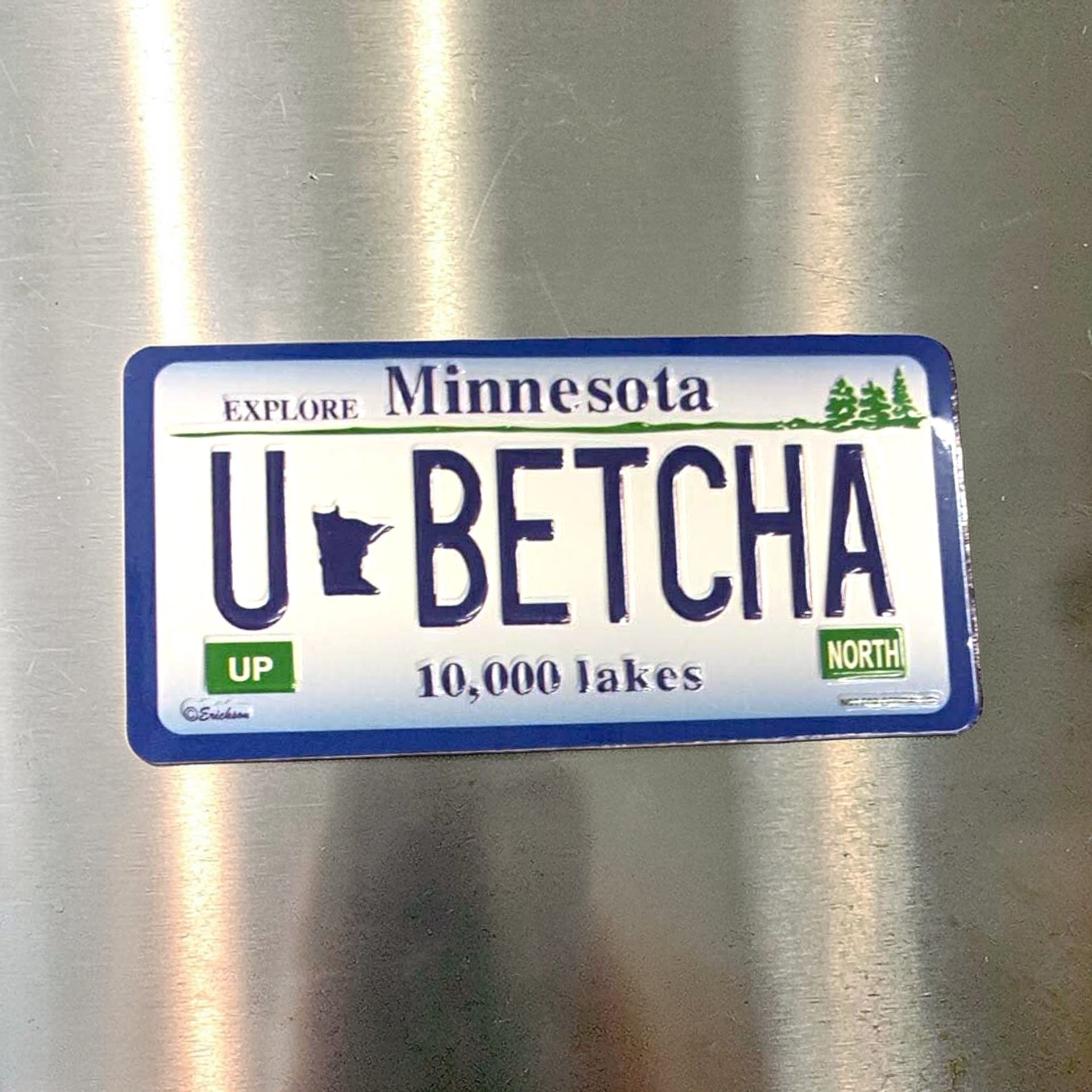 Minnesota-themed license plate sticker with 'U BETCHA' on a metallic surface