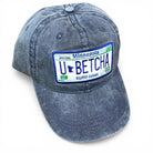 Blue denim cap with a Minnesota-themed license plate design that states “u betcha!” on a white background