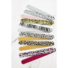 An assortment of ten glittery and patterned emery board nail files fanned out on a white marble background, featuring zebra stripes, cheetah print, and hot pink leopard print.