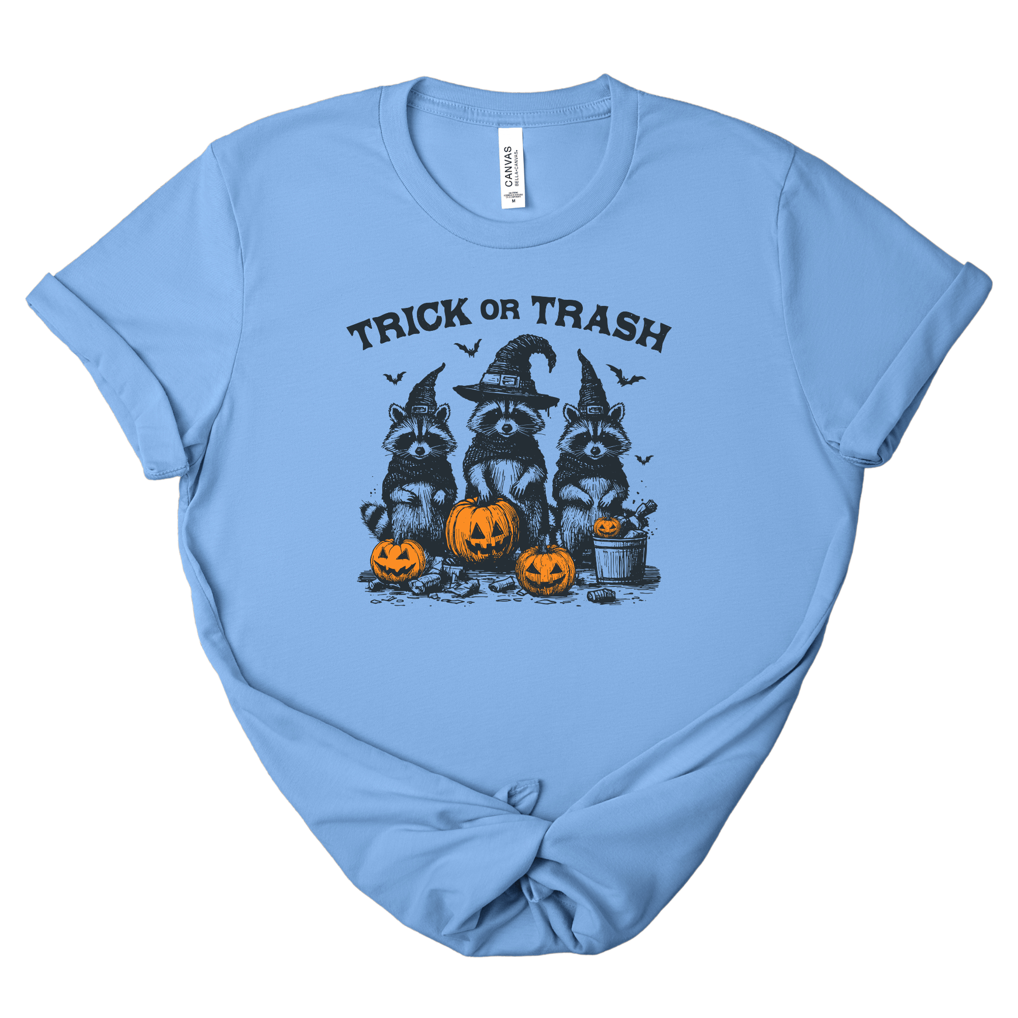 A light blue short-sleeve t-shirt with a 'Trick or Trash' Halloween graphic featuring raccoons in witch hats and jack-o'-lanterns, displayed flat against a white background.
