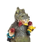 A comical figurine of a dinosaur holding two garden gnomes in its mouth and arms. The gnomes are wearing colorful outfits and appear surprised.