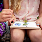 Two children holding a small digital tablet with images of flowers on its screen.