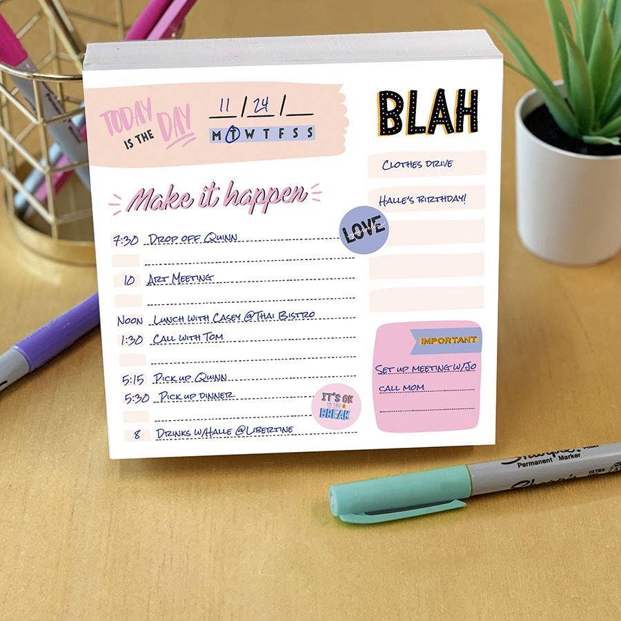 A colorful daily planner on a wooden desk, titled "Make it happen," lists various tasks with times. Nearby are a pen holder, marker, and potted plant.