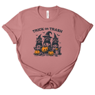 A dusty rose short-sleeve t-shirt with a 'Trick or Trash' Halloween graphic featuring three raccoons in witch hats and jack-o'-lanterns, laid flat on a white background.