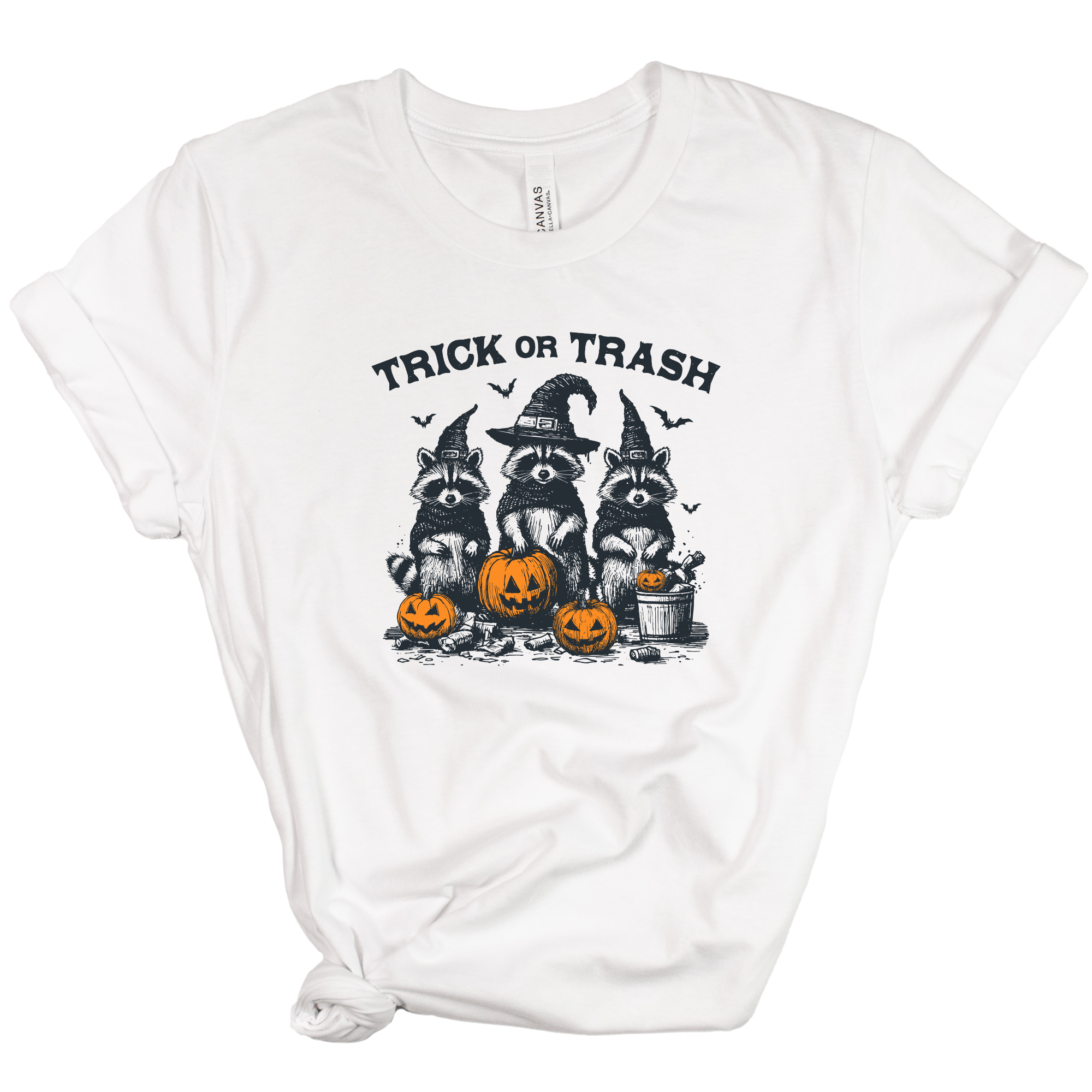 A white short-sleeve crewneck t-shirt with a graphic of three raccoons dressed as witches holding pumpkins, with the text 'TRICK OR TRASH' above them.