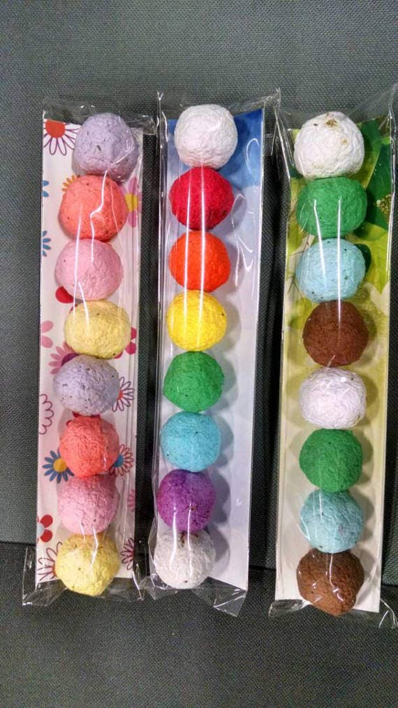 Three plastic-wrapped strings of colorful textured balls are displayed vertically. Each string has pastel and bright hues on floral and abstract backings.