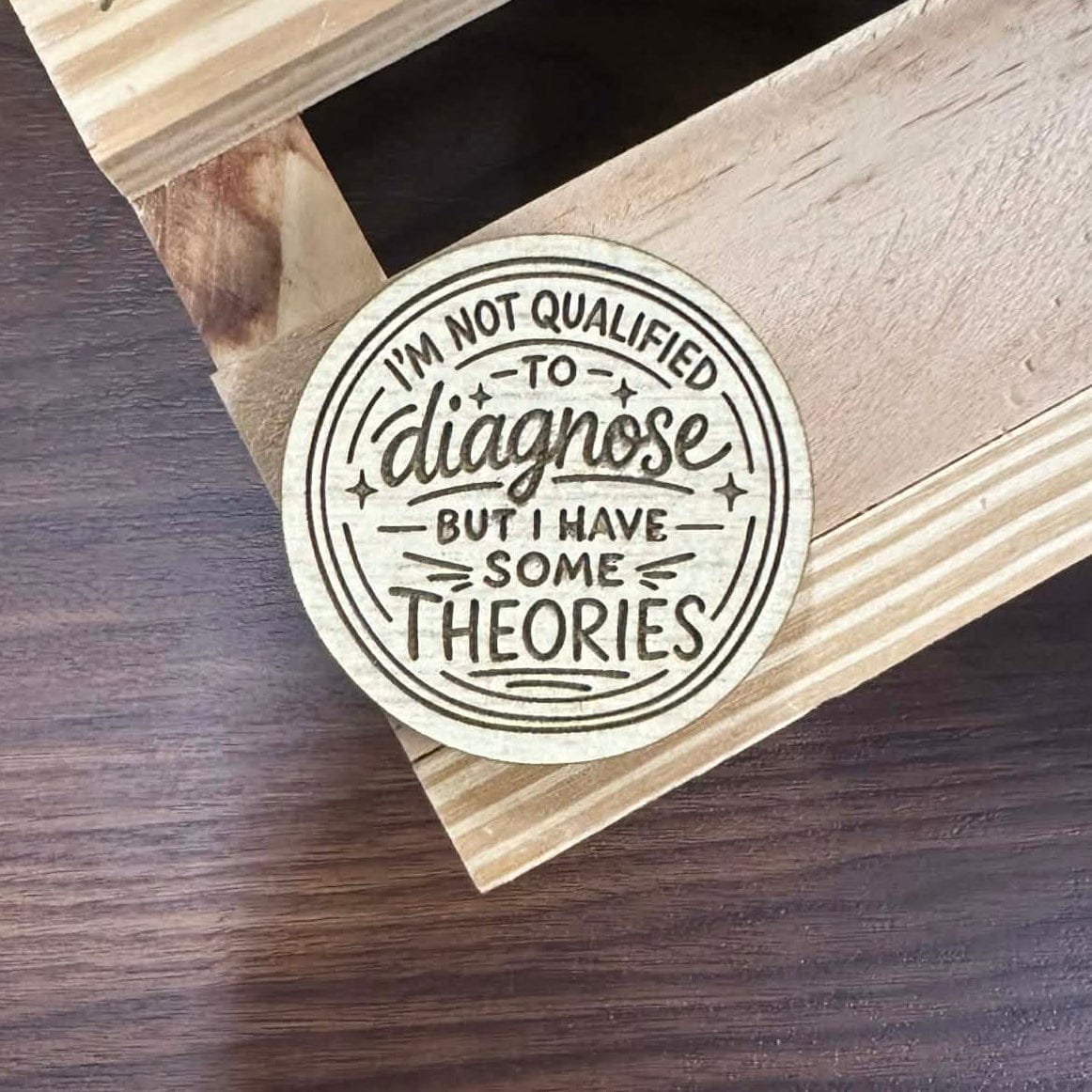 Circular sticker with text on a wooden surface.Text states "I'm not qualified to diagnose, but I have some theories."