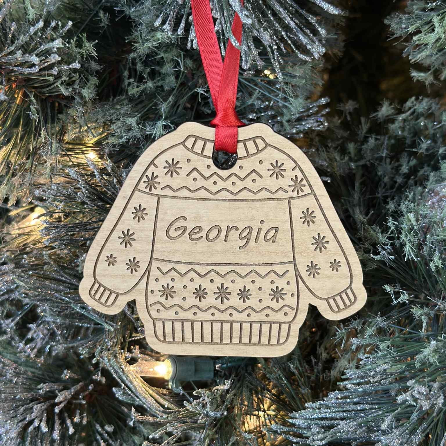 Decorative ornament shaped like a sweater with 'Georgia' on it, hanging on a Christmas tree.
