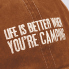 Close-up of a brown fabric, possibly a cap, with white embroidered text reading "Life is better when you're camping," conveying a sense of outdoor adventure and relaxation.