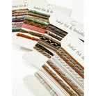 Assorted hair ties and bracelets arranged on white cards. Each card displays various designs and colors, from braided textures to solid hues, creating a vibrant and playful tone.