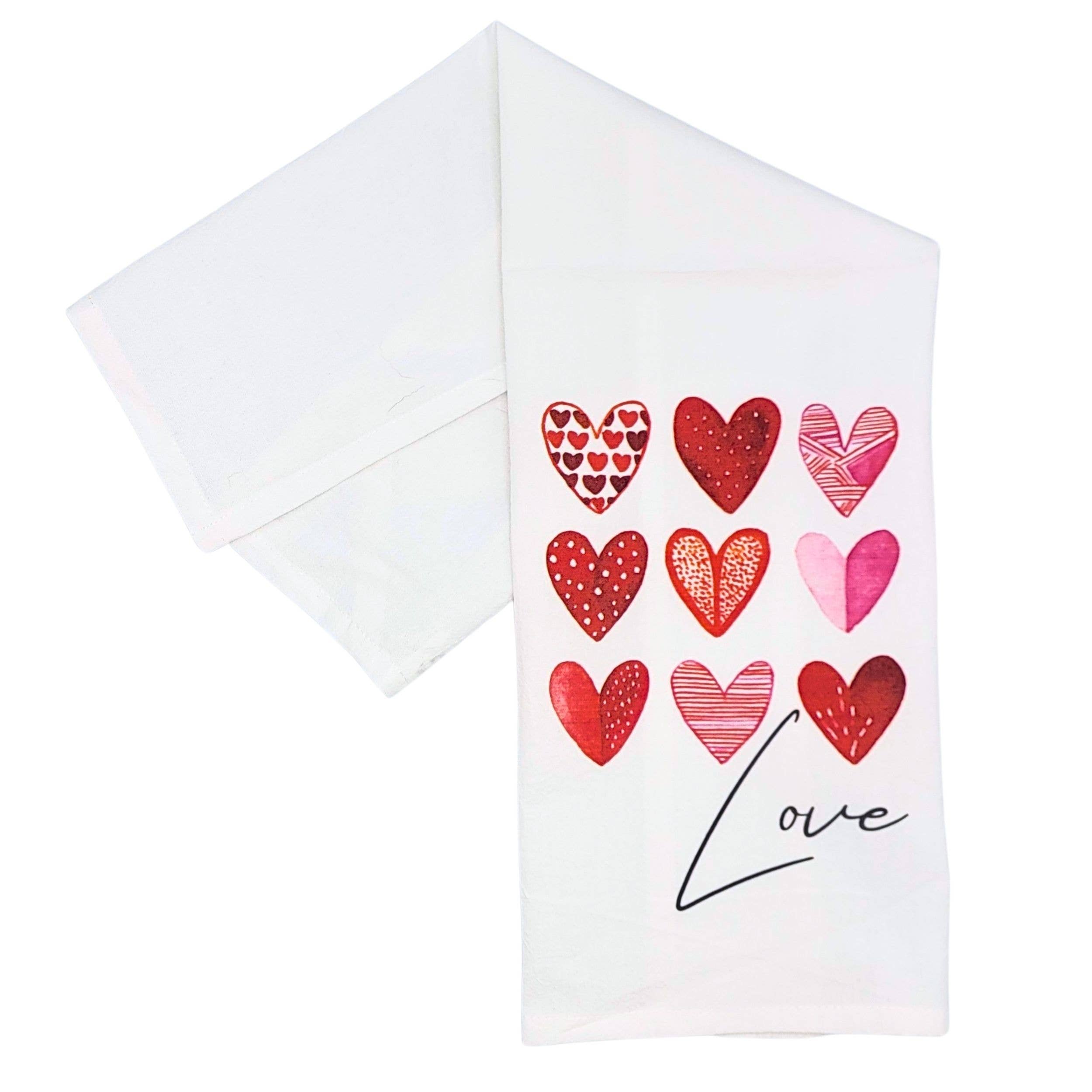 White towel with a nine-patterned red heart design in rows. "Love" is scripted beneath the hearts. A theme of affection and warmth is conveyed.