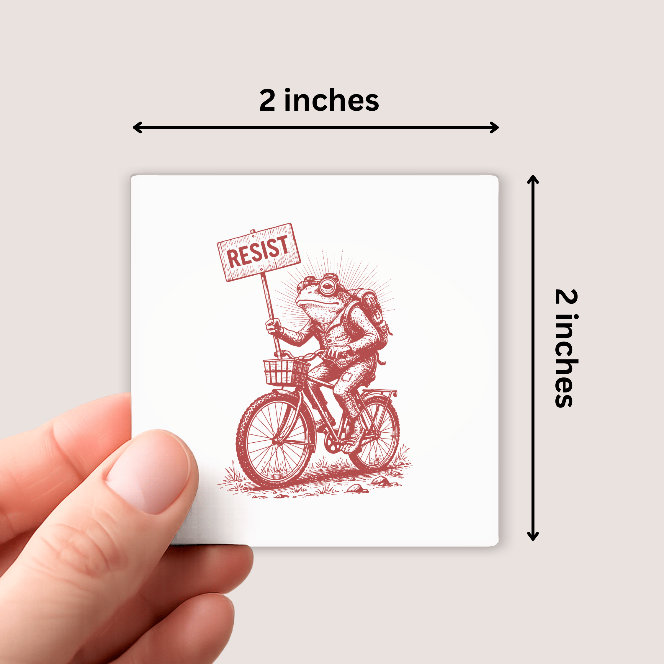 Small card with a red illustration of a frog on a bicycle holding a 'Resist' sign, held by a hand against a light gray background.
