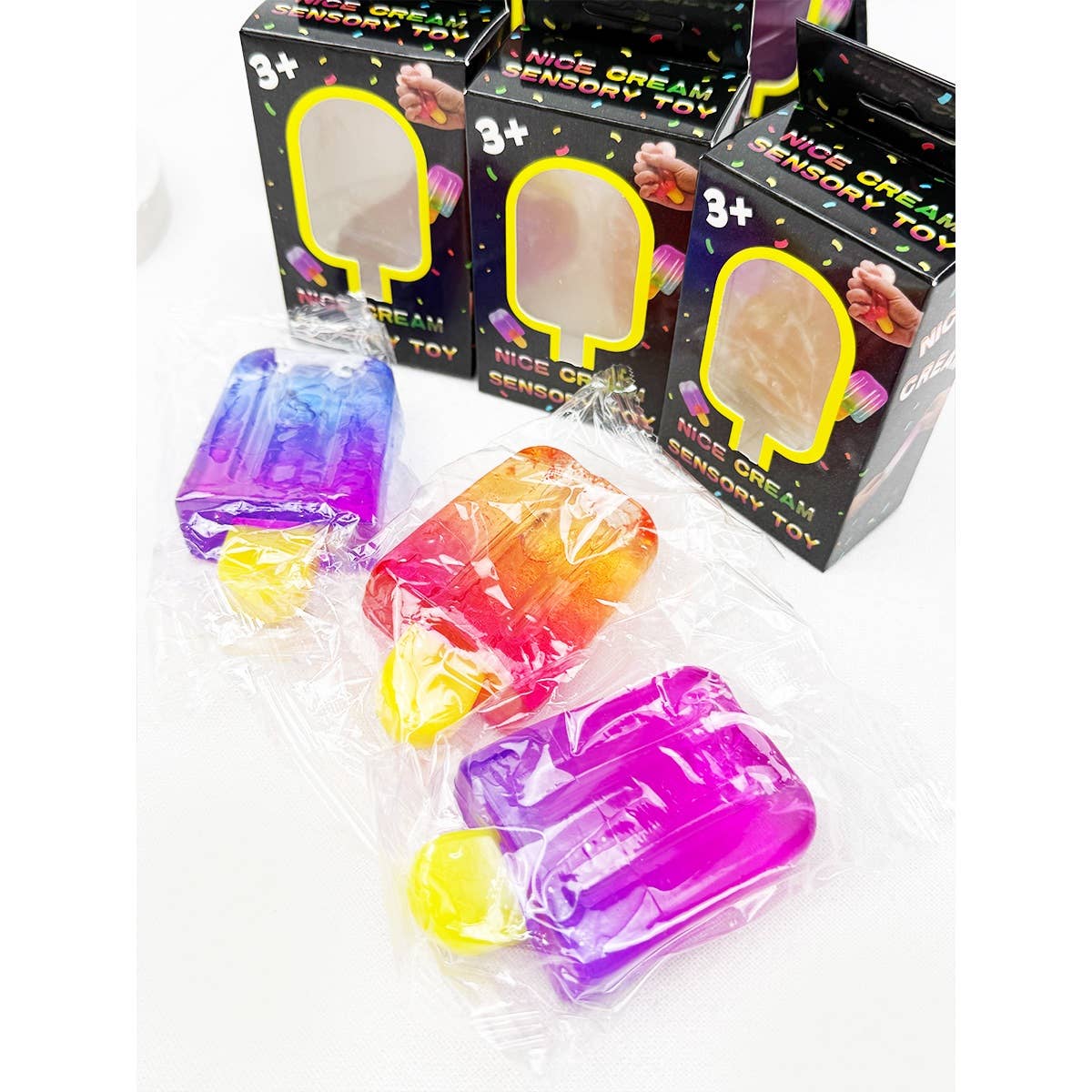 Three popsicle-shaped ice cream bar squeeze squishy sensory toys in translucent purple, blue, and pink/orange gradient colors next to their retail boxes.