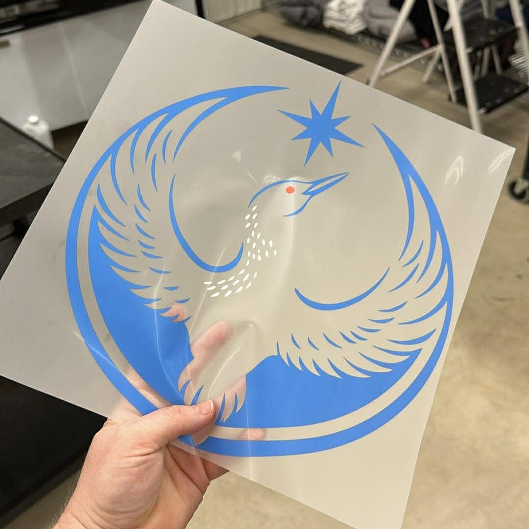 Hand holding a DTF print of the rebel loon design with blue and white colors in an indoor setting.