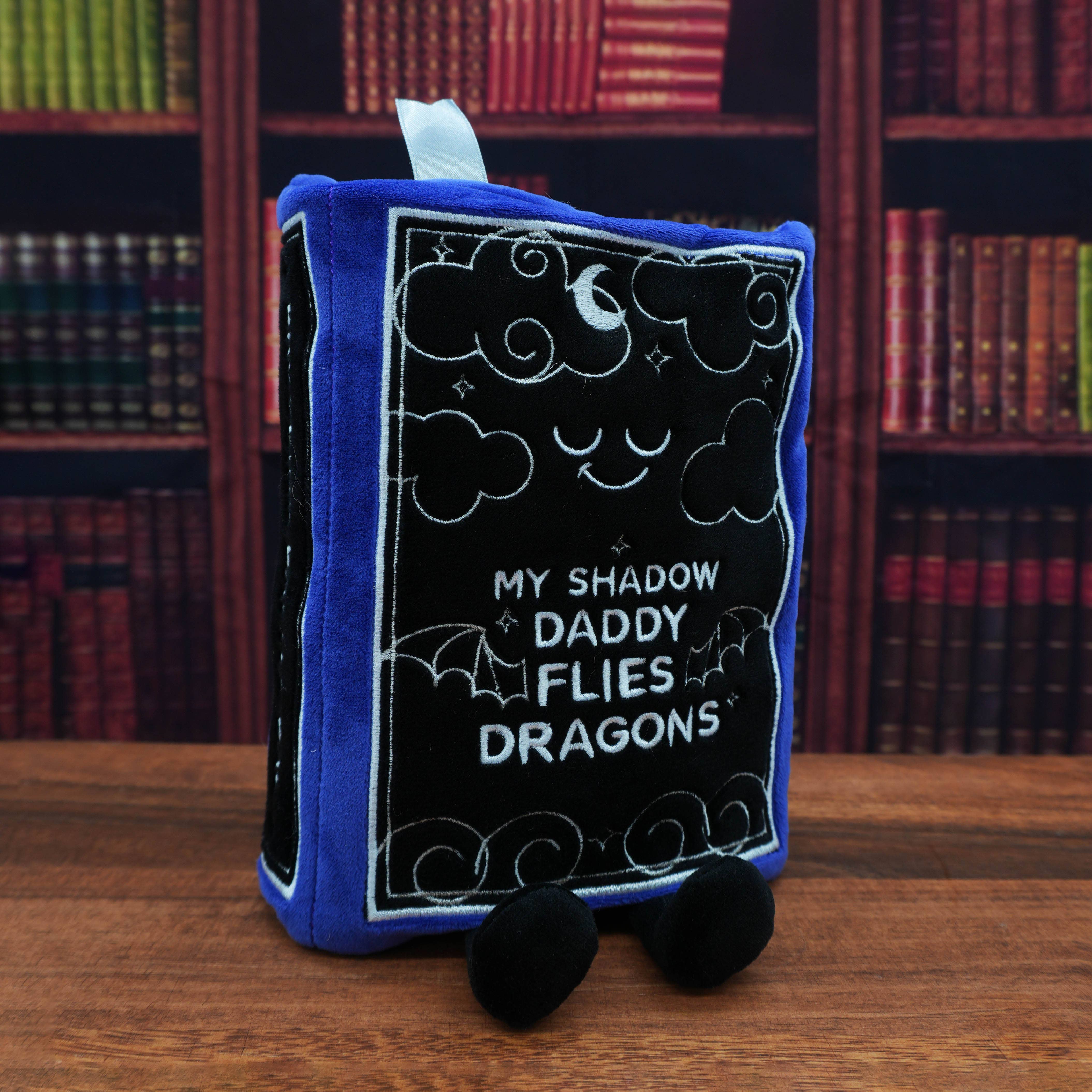 Plush book-shaped toy with text in front of a bookshelf
