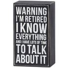 A square black wooden box sign with a distressed finish and white text that reads: 'WARNING I’M RETIRED I KNOW EVERYTHING AND I HAVE LOTS OF TIME TO TALK ABOUT IT.