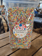 A clear plastic bag filled with colorful shredded paper labeled "DIY Wildflower Seed Bombs" sits on a wooden table, suggesting creativity and gardening fun.