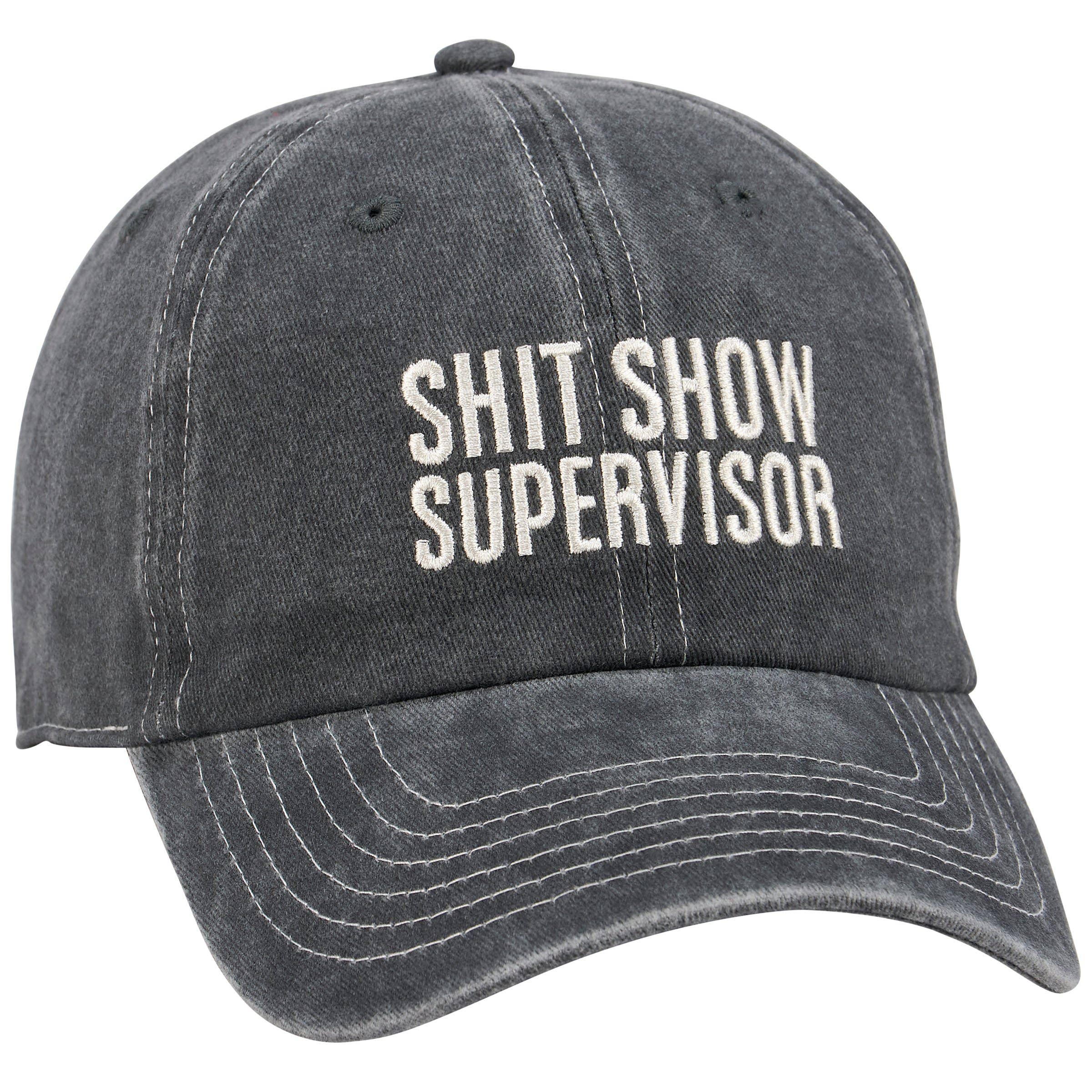 A stonewashed black baseball cap featuring cream-colored embroidered text on the front that reads 'SHIT SHOW SUPERVISOR' in a capitalized serif font. The hat has a distressed, vintage look with an adjustable metal buckle in the back.