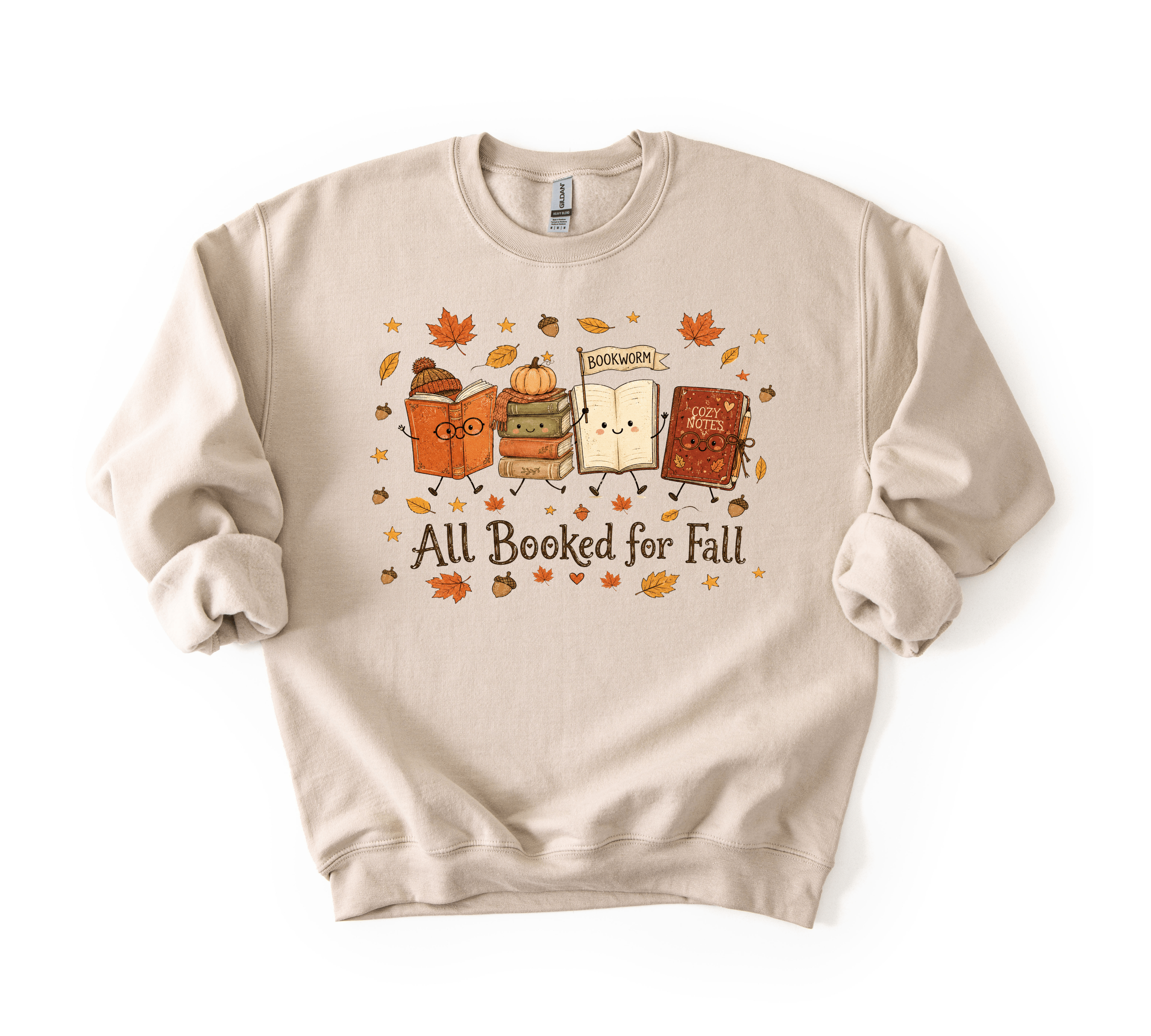 A beige crewneck sweatshirt featuring a cute autumn-themed graphic of three books with faces, surrounded by falling leaves and acorns, with the text 'All Booked for Fall' printed below.