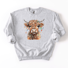 Gray sweatshirt with a colorful highland cow illustration wearing Christmas lights on a white background