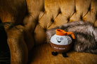 A brown and white coffee pot plushie with an orange pour spout. The white portion has a smiley face, and the brown portion features white text that says "Pot Head." The plushie has black legs sticking out.