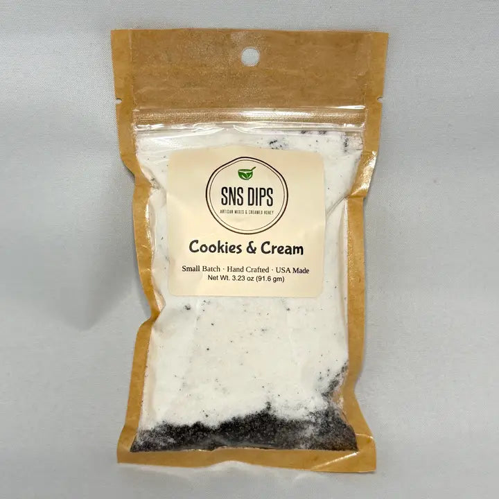 A brown, transparent package labeled "Cookies & Cream" from SNS Dips. It contains a white powder with dark specks, indicating a sweet mix.