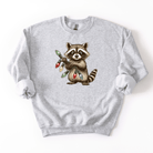 Gray sweatshirt with a raccoon holding Christmas lights design on a white background