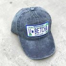 Blue cap with a Minnesota-themed license plate design that states “u betcha” on a concrete surface. 
