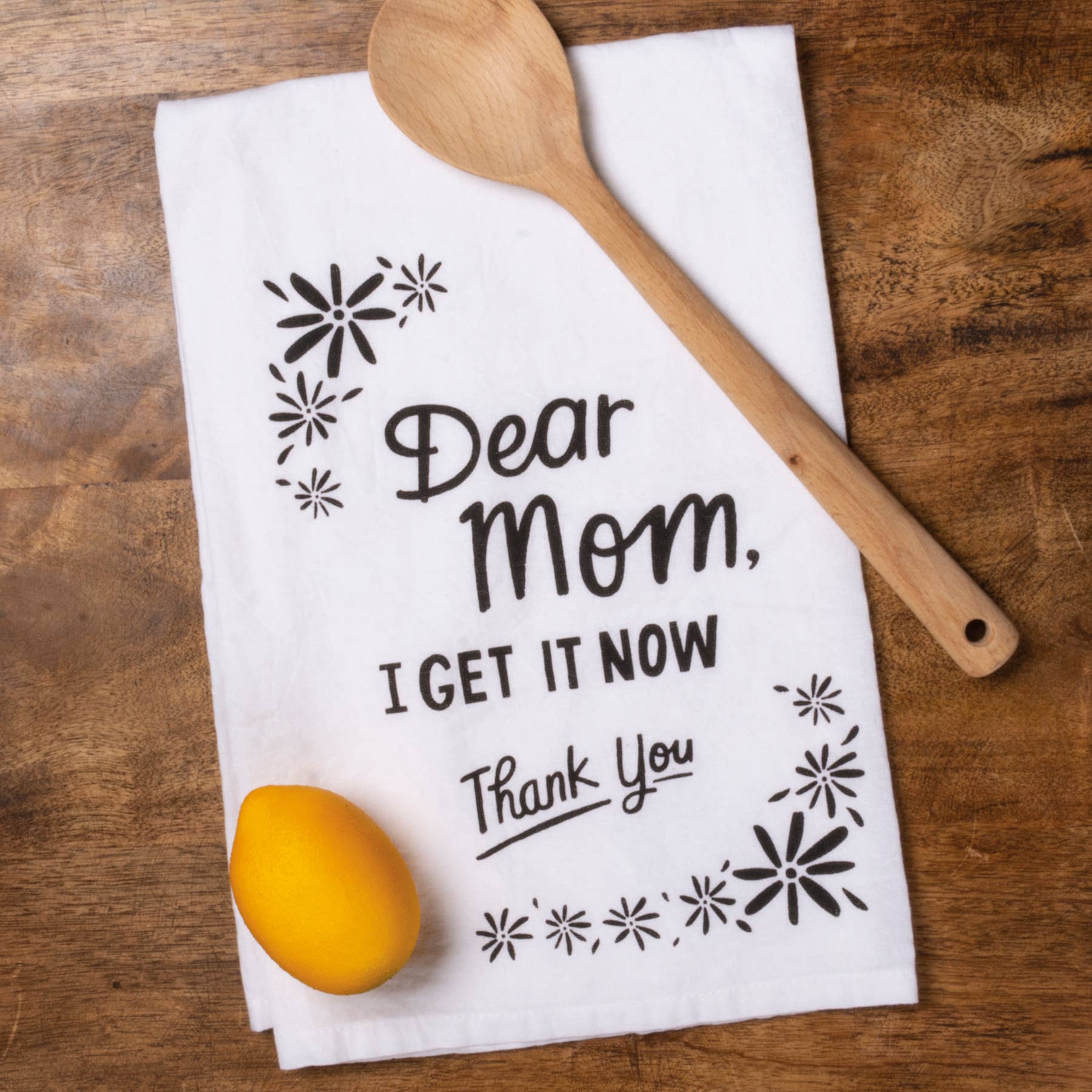 A black and white cotton kitchen towel featuring a "Dear Mom, I Get It Now Thank You" sentiment with floral designs.