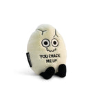 A white cracked egg plush with a squiggly smiley face and black text that says "You crack me up." The plushie has black legs sticking out.