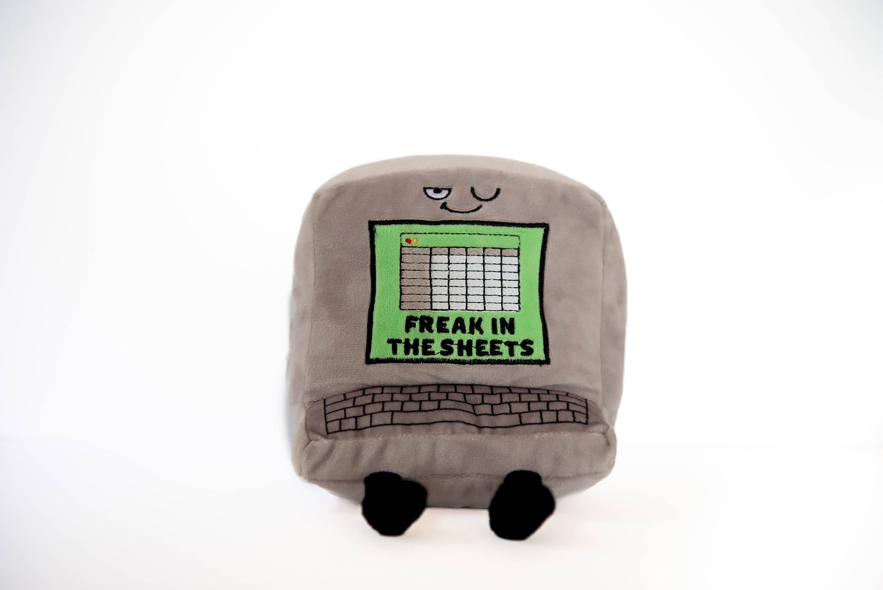 A gray computer plush with a winky face, featuring a green Excel-style sheet embroidered with the words "Freak in the Sheets" in black. It also has an outlined keyboard design and black legs sticking out from the bottom.