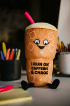 Plushie shaped like a ln iced coffee with a cute face that reads “ I run on caffeine and chaos”