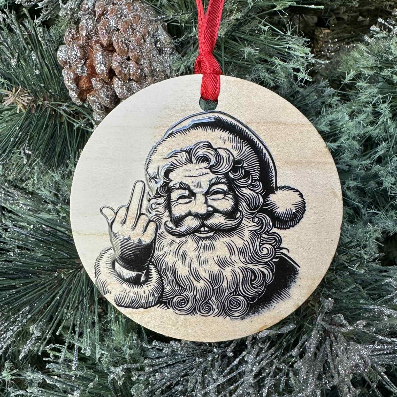 Wooden Christmas ornament with a humorous Santa Claus design giving a middle finger, hanging on a tree.