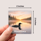Fridge magnet with a scenic image of a lake and trees, held by a hand, with dimensions indicated.
