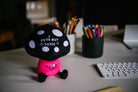 A mushroom plush with a black and white polka dot top and white text that says "Cute but toxic." The stem is pink with a winking smiley face, and the plushie has black legs sticking out.