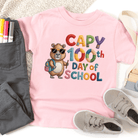 Pink t-shirt with a bear graphic and 'Capy 100th Day of School' text, surrounded by casual items.