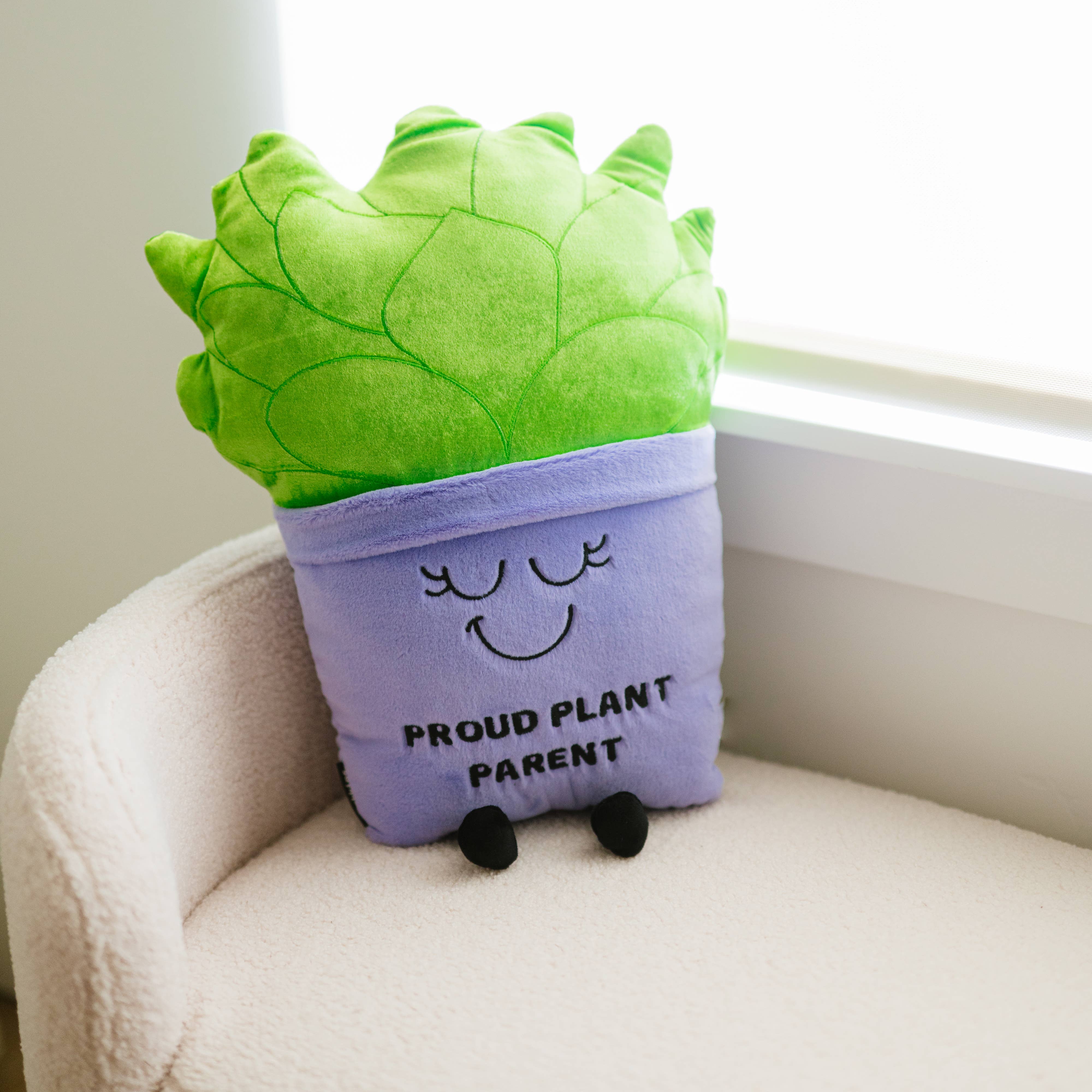 A soft, plush plant toy featuring a vibrant green plant in a purple pot. The pot has a cheerful, smiling face with closed eyes, and black text on the front reads 'Proud Plant Parent.'